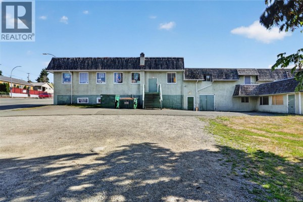 Rear view of a long, light green commercial building with an exterior staircase and dumpster. - 3304 3rd Ave, Port Alberni