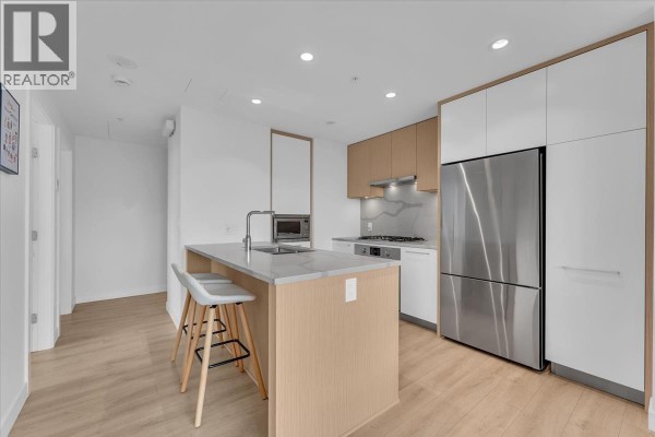 Spacious kitchen with island, stainless steel refrigerator, white and wood cabinetry, and light wood flooring. - 3305 567 Clarke Road, Coquitlam