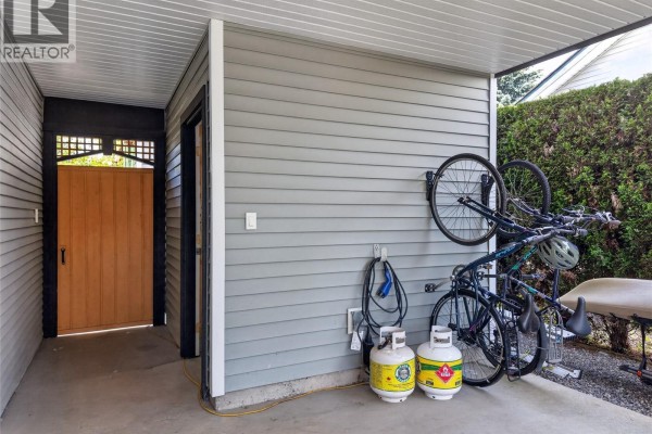 Covered outdoor storage area with two bicycles mounted on the wall, propane tanks, and a wooden gate. - 3305 Ninth St, Cumberland