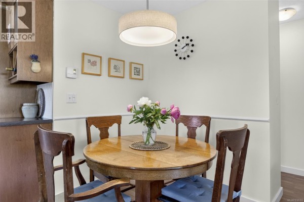 Round wooden dining table with four chairs and a vase of pink and white peonies in a dining nook. - 3305 Ninth St, Cumberland