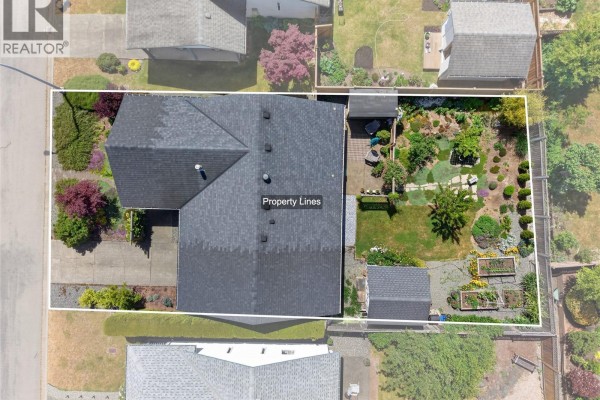 Aerial view of a residential property with a dark roof, fenced yard, garden beds, and a detached shed. - 3305 Ninth St, Cumberland