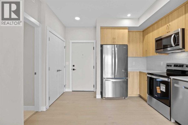 View of the kitchen from the hallway entrance showing appliances and cabinetry. - 3306, 100 Banister Drive, Okotoks