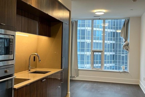 A modern kitchen counter with stainless steel appliances and a sink next to a living area with a large window. - 3306 - 10 York Street, Toronto