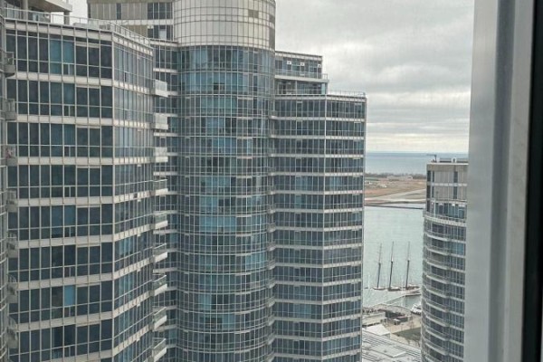 View from apartment window showing multiple glass towers, a body of water, and a cloudy sky. - 3306 - 10 York Street, Toronto