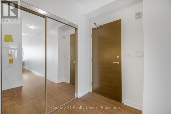 Interior hallway with a wooden door, mirrored closet doors, and view into living area. - 3307 - 21 Iceboat Terrace, Toronto