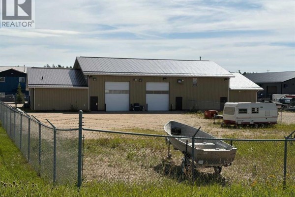 Rear exterior of commercial building with two white garage doors, fence, and a boat on trailer. - 3307 41 Avenue, Whitecourt