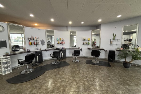 Wide view of salon styling stations with chairs, mirrors, and product shelves on the wall. - 3309 Portage Avenue, Winnipeg