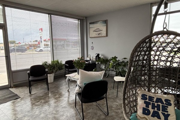 Salon waiting area with black chairs, a hanging rattan chair, plants, and large windows. - 3309 Portage Avenue, Winnipeg
