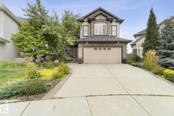 Front exterior of a two-story house with a paved driveway, stone facade, and landscaping during the day. - 331 Callaghan Cl Sw, Edmonton