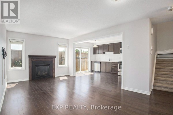 Living room with fireplace and dark hardwood floors, opening to a kitchen area with a sliding glass door to the backyard. - 331 Willow Aster Circle, Ottawa