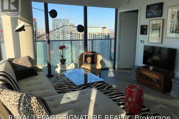 A living room with large windows showcasing a city view, a sofa, armchair, and wall art. - 3310 - 161 Roehampton Avenue, Toronto