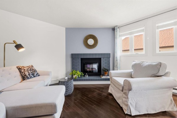 Living room with a fireplace, two sofas, and windows showing a roof view. - 3311 65 Swindon Way, Winnipeg