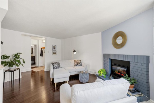 Living area with white sofas, fireplace, dark wood floors, and an open doorway to the bathroom. - 3311 65 Swindon Way, Winnipeg