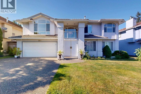 Side exterior view of the large, light blue house showing a sloping green lawn and mature trees. - 3311 Rakanna Place, Coquitlam
