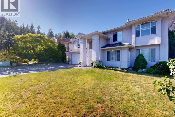 Front view of the house from the driveway, showing the concrete driveway, lawn, and neighboring houses. - 3311 Rakanna Place, Coquitlam