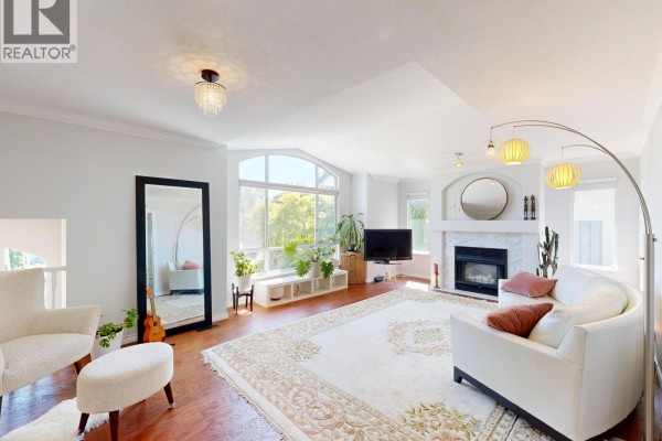 Living room with hardwood floors, white sofa, fireplace, large window, and ornate rug. - 3311 Rakanna Place, Coquitlam