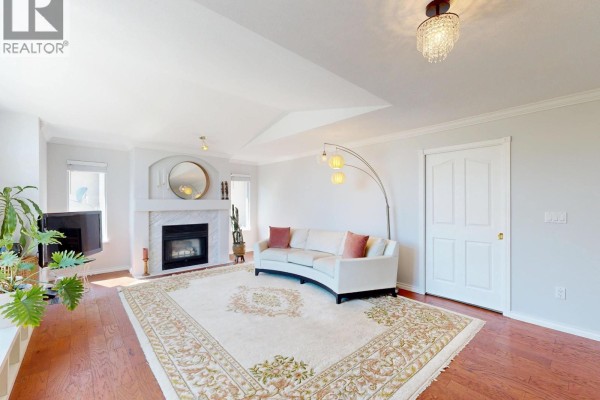 Living room with a fireplace, white sofa, hardwood floors, and a large decorative rug. - 3311 Rakanna Place, Coquitlam