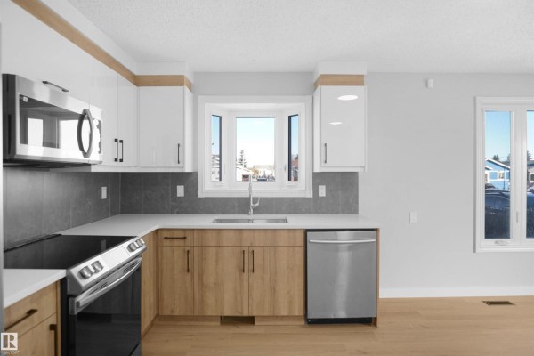 Modern kitchen with stainless steel appliances, white cabinets, and gray backsplash. - 3312 44a St Nw, Edmonton