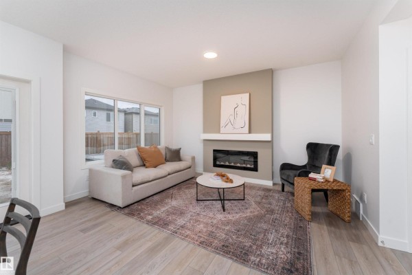 Living room with a light grey sofa, dark armchair, marble coffee table, and electric fireplace. - 332 27 St Sw, Edmonton
