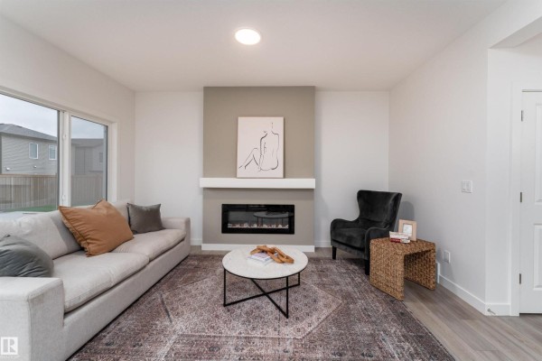 Living room showcasing a neutral sofa, dark armchair, round coffee table, and decorative fireplace. - 332 27 St Sw, Edmonton
