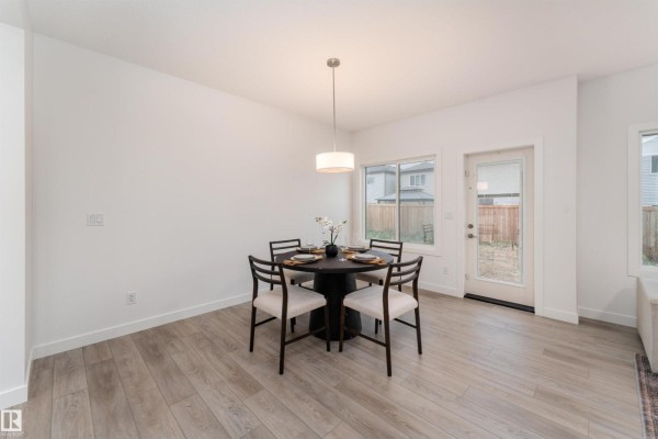 Dining area with a round table set for four, pendant light, and a door to the backyard. - 332 27 St Sw, Edmonton