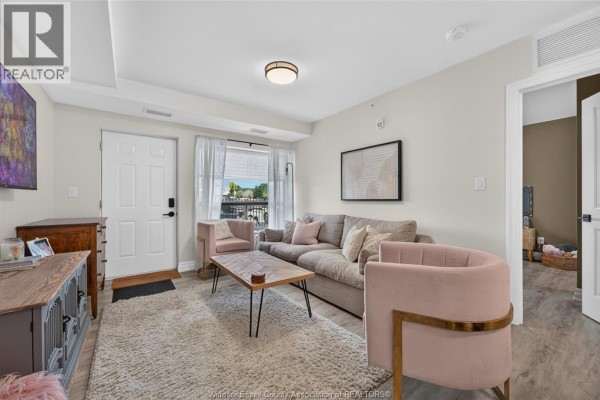 Living room with a sofa, pink chairs, coffee table, a closed door, and an open doorway to another room. - 3320 Stella Crescent Unit# 109, Windsor