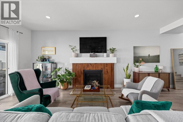 Open concept living area with a grey sofa, fireplace, dining area, and kitchen island. - 3321 Hawks Crescent, Westbank