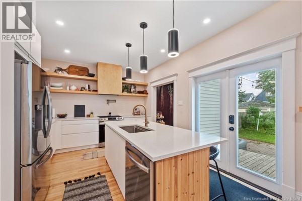 Modern kitchen with white cabinets, an island, stainless steel appliances, and a back door view. - 333 Cameron Street, Moncton
