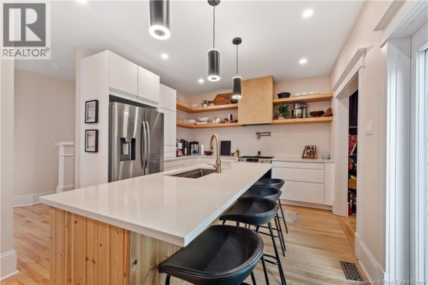 Kitchen island with seating for four, surrounded by white cabinets and modern pendant lights. - 333 Cameron Street, Moncton