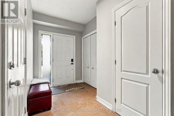 Foyer with beige tiled floor, white front door, and double closet doors. - 333 Riversedge Crescent, Ottawa