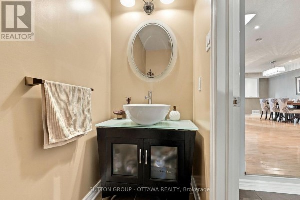 Powder room with a beige vanity, vessel sink, oval mirror, and towel rack. - 333 Riversedge Crescent, Ottawa