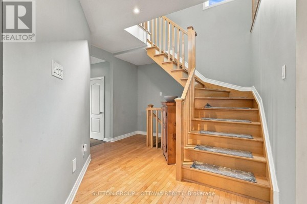 Hallway with light grey walls, hardwood floors, and a wooden staircase with carpeted treads. - 333 Riversedge Crescent, Ottawa