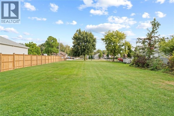 Expansive view of a green, vacant lot bordered by a wooden fence and surrounded by suburban homes. - 333 Victoria Street, Essex