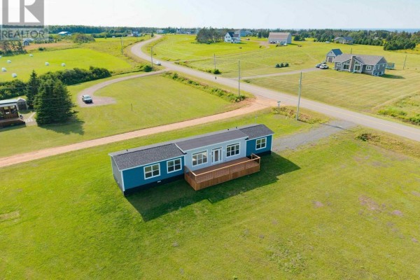 Aerial view of a blue mobile home with a deck in a rural waterfront setting. - 3334 Wild Harbour Road, Wildharb
