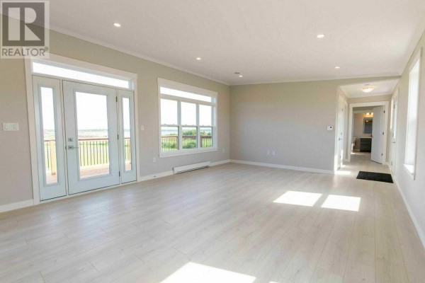 Living room with light wood floors, white trim, and large windows overlooking the water. - 3334 Wild Harbour Road, Wildharb
