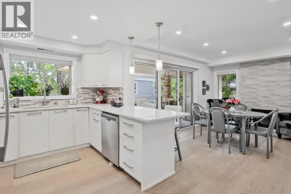 Open concept kitchen and dining area with white cabinets, quartz countertops, and light wood flooring. - 3335 Richter Street Unit# 201, Kelowna