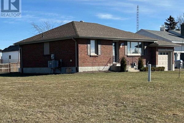 Side view of a red brick bungalow showing the front door, garage, and grassy yard. - 33374 Richmond Street, Lucan Biddulph