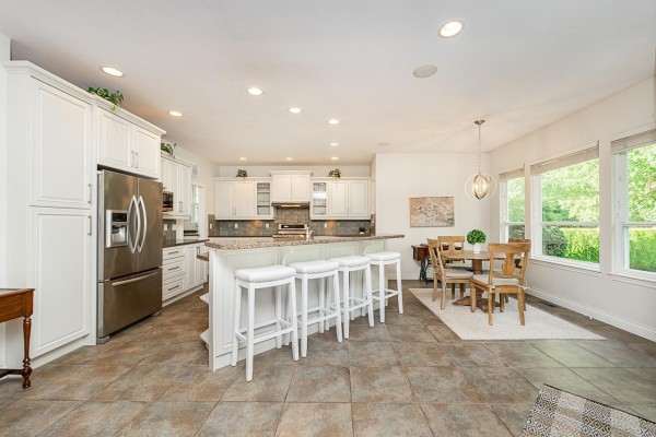 White kitchen with stainless steel appliances, granite countertops, island with bar stools, and adjacent dining area. - 3338 157a Street, Surrey