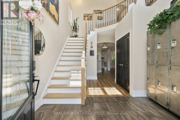 Interior foyer with a grand staircase, light wood floors, and dark doors, viewed from the entrance. - 334 Blacksmith Way, Peterborough