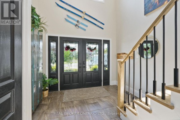 Interior foyer with a double front door, a staircase with black railings, and decorative skis on the wall. - 334 Blacksmith Way, Peterborough