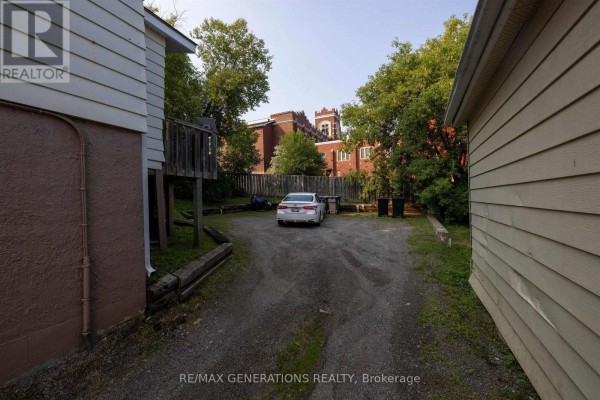 Gravel driveway with a white car parked, leading towards a brick building behind trees. - 334 Pearl Street, Thunder Bay