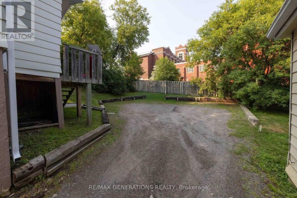 View of a gravel area between two houses with wooden borders and lush green trees. - 334 Pearl Street, Thunder Bay
