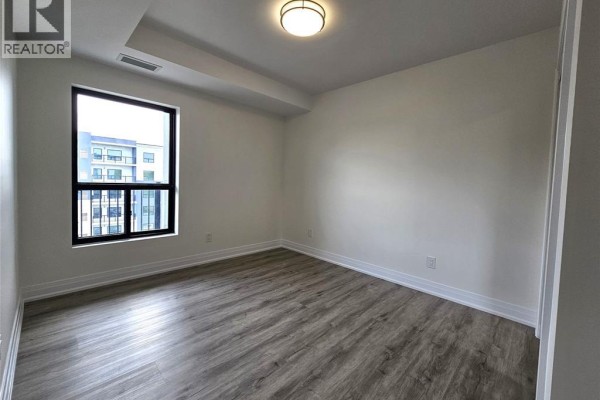 Empty room with grey wood-look flooring and a large window with a view of an apartment building. - 3340 Stella Crescent Unit# 517, Windsor