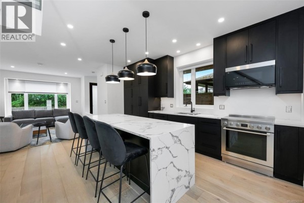 Modern kitchen with black cabinetry, white marble island with bar stools, stainless steel appliances, and pendant lighting. - 3341 Skinner Rd, Duncan