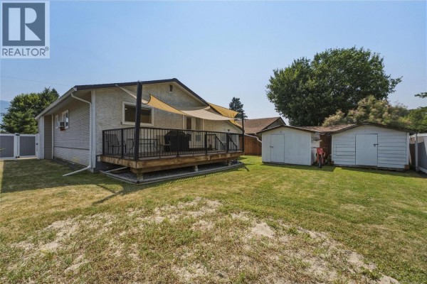 Backyard view with a wooden deck, two white sheds, a large green lawn, and a vinyl fence. - 3343 Belaire Drive, Armstrong