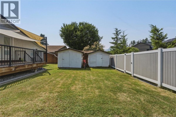 View of the backyard with two white sheds, green grass, and a beige vinyl privacy fence. - 3343 Belaire Drive, Armstrong