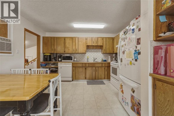 Spacious kitchen with light wood cabinets, white appliances, tiled floor, and a dining table in the foreground. - 3343 Belaire Drive, Armstrong