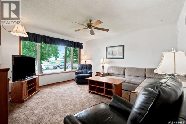 Living room with sectional sofa, armchair, coffee table, and large window. - 335 Broad Street, Lumsden