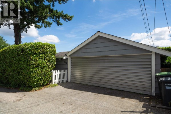 Exterior of a detached garage with a grey roller door, white picket gate, and green hedges. - 335 Churchill Avenue, New Westminster