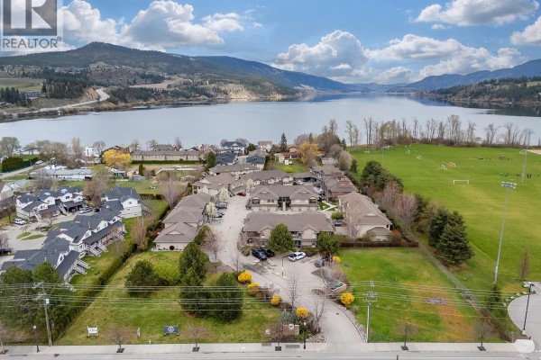 Aerial view of a townhouse complex with a lake and mountains in the background. - 3350 Woodsdale Road Unit# 401, Lake Country